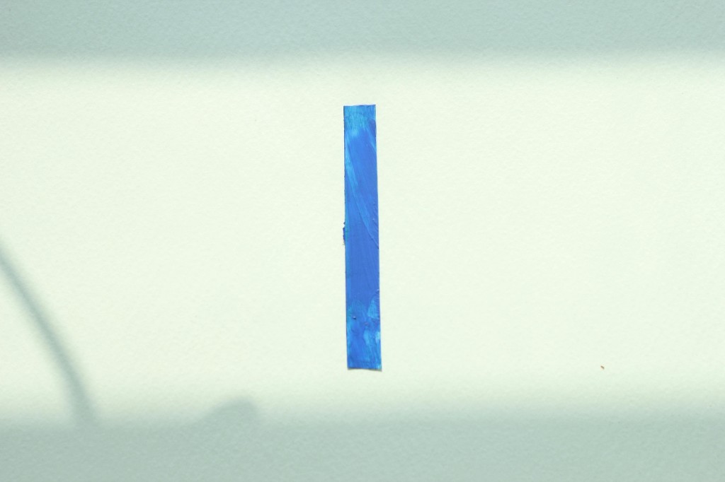 Abstract minimalist image with a vertical stroke of textured blue paint on a light neutral background.